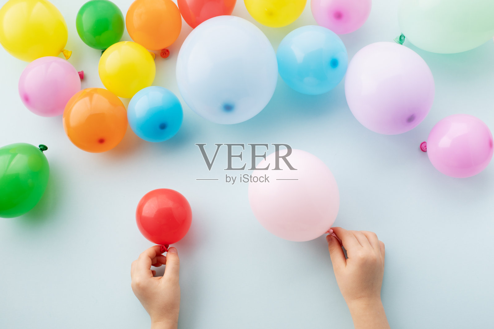 孩子的手握着气球，周围散落着许多气球，背景是蓝色的节日氛围。这是儿童生日、庆祝和派对的概念。照片摄影图片