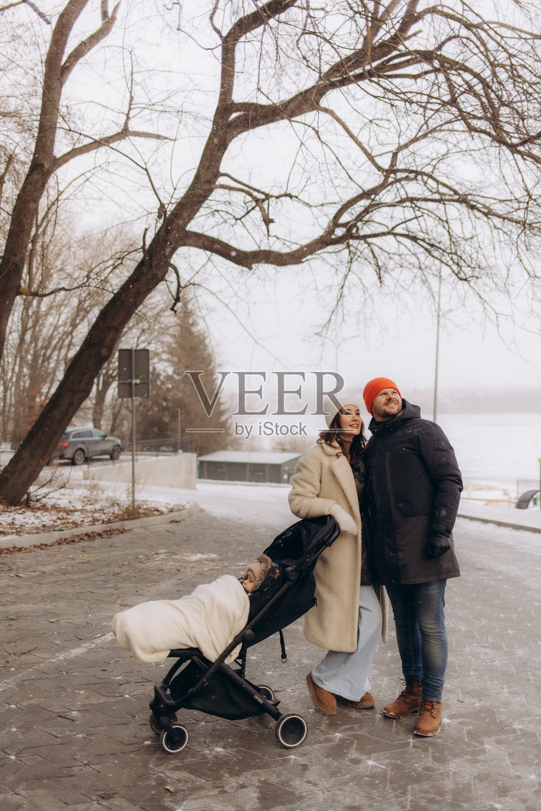 冬天，父母推着婴儿车带着孩子散步。快乐的父母，雪花纷飞。照片摄影图片
