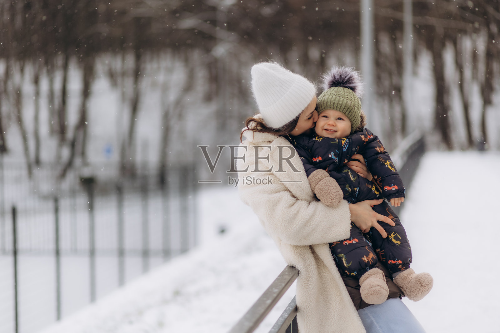 一位穿着白色衣服和白色帽子的母亲在冬季户外抱着她的儿子。快乐的人们。照片摄影图片