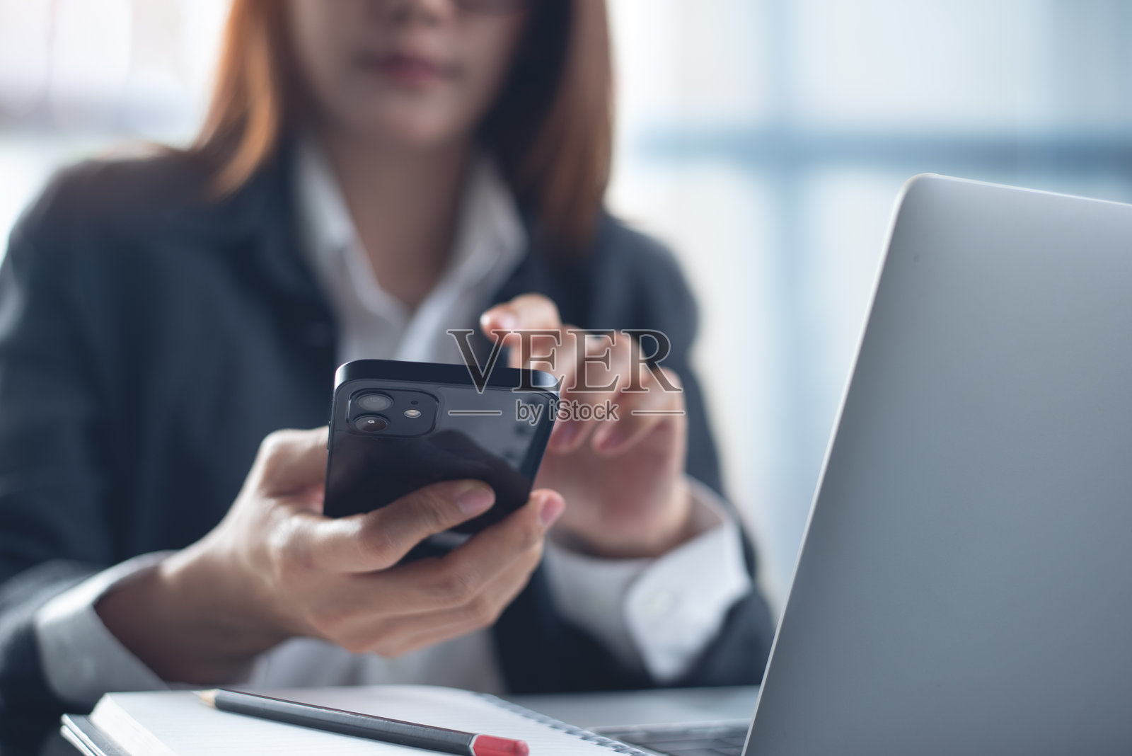 年轻聪明的女商人在现代办公室使用手机和笔记本电脑工作。亚洲女商人使用智能手机搜索信息，浏览互联网，企业商务概念。照片摄影图片