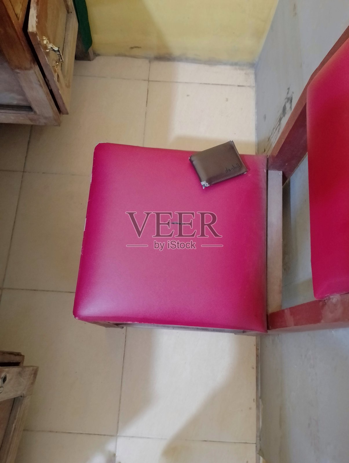 在简单的房间环境中，遗失的钱包被遗忘在一把亮粉色的椅子上照片摄影图片