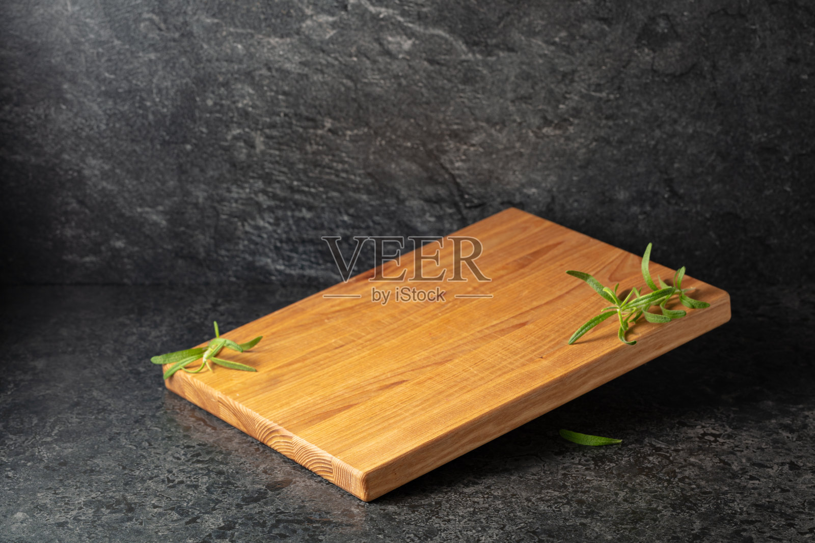 黑色石材背景上的空切菜板和迷迭香。照片摄影图片