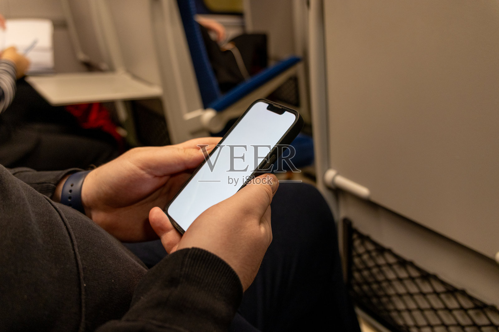 在晚间旅途中，坐在火车座位上的人手持一部空白白屏的智能手机照片摄影图片