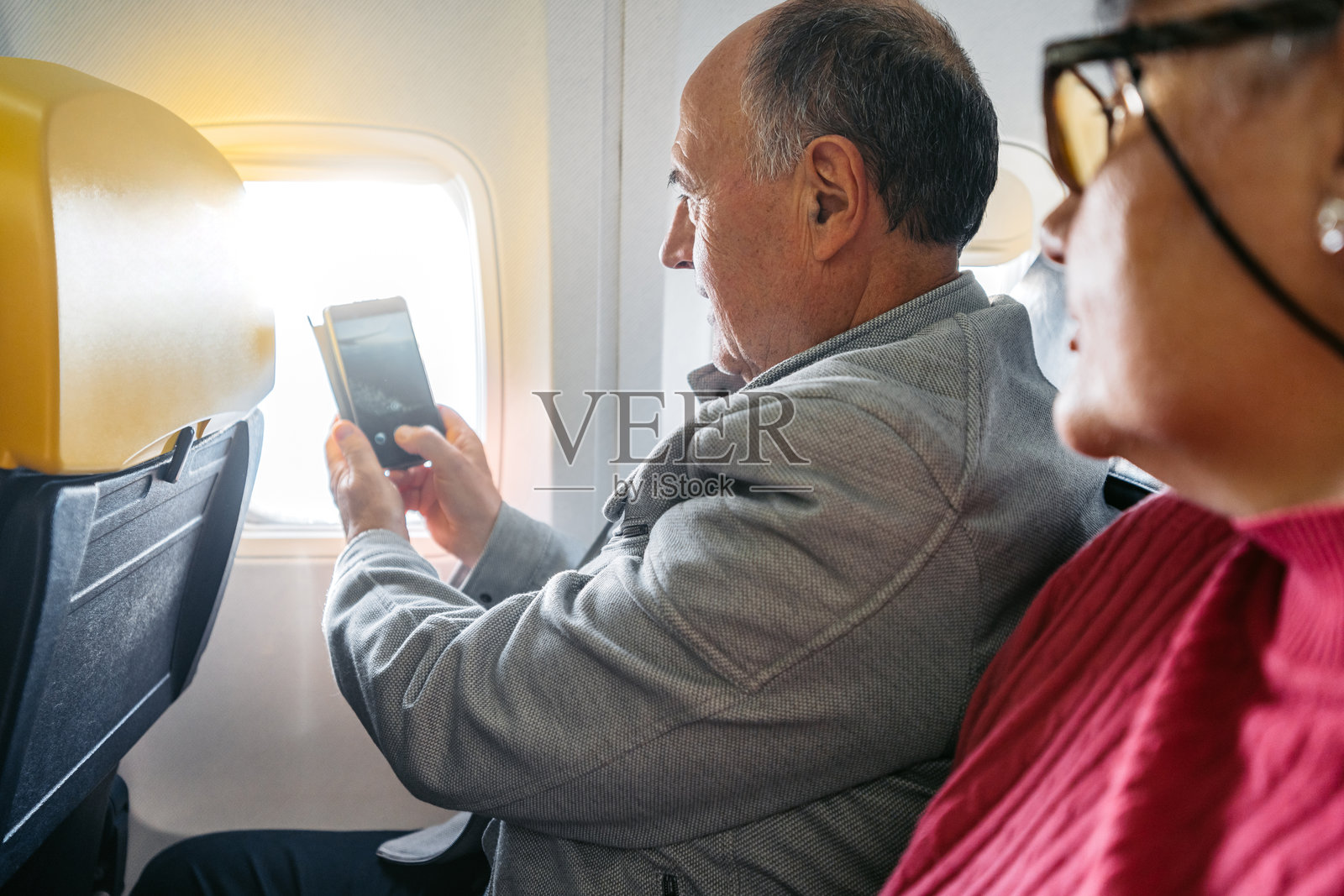 老年夫妇用手机拍摄飞机窗外的风景照片摄影图片