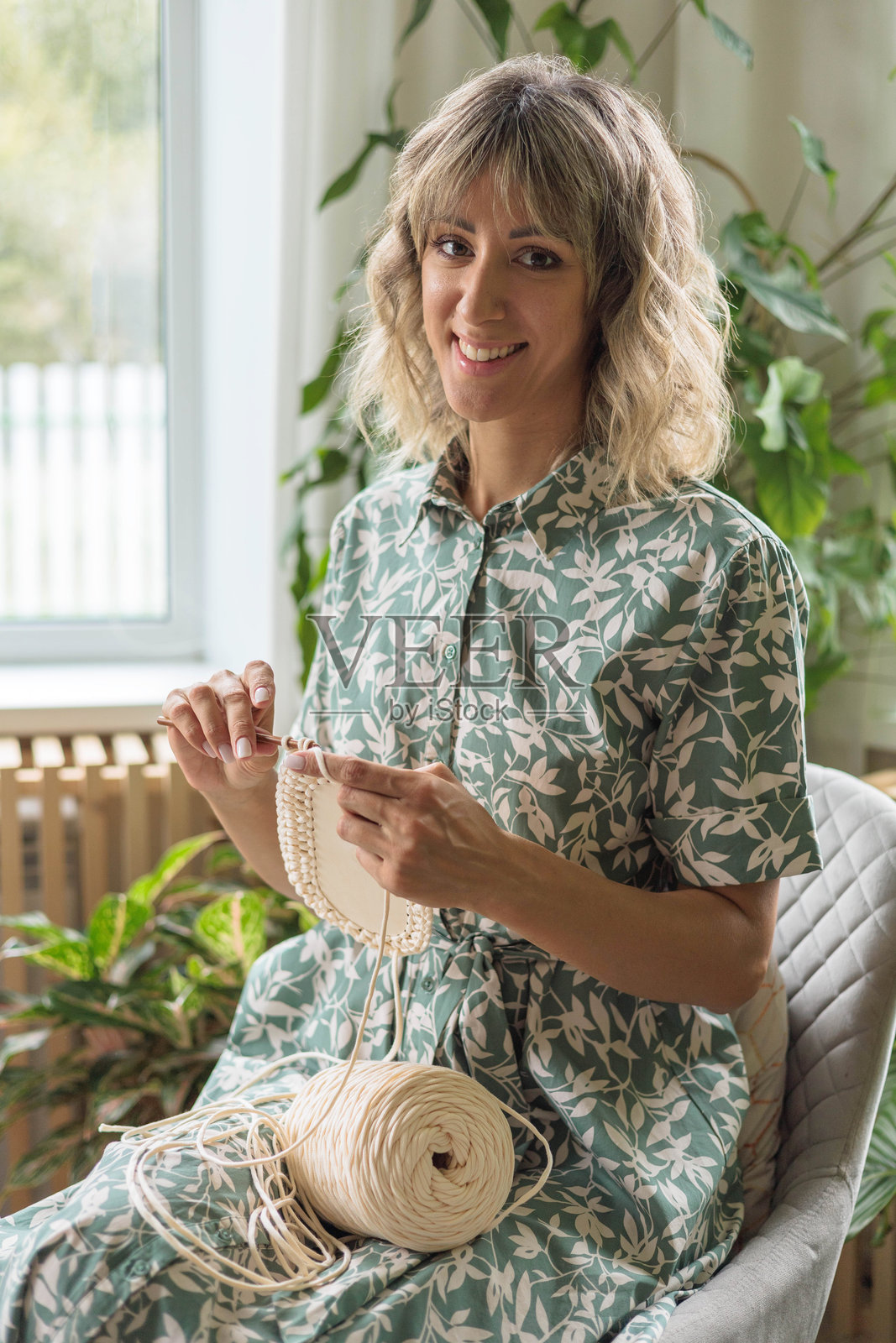 年轻美丽的欧洲女孩用米色纱线编织储物篮。照片摄影图片
