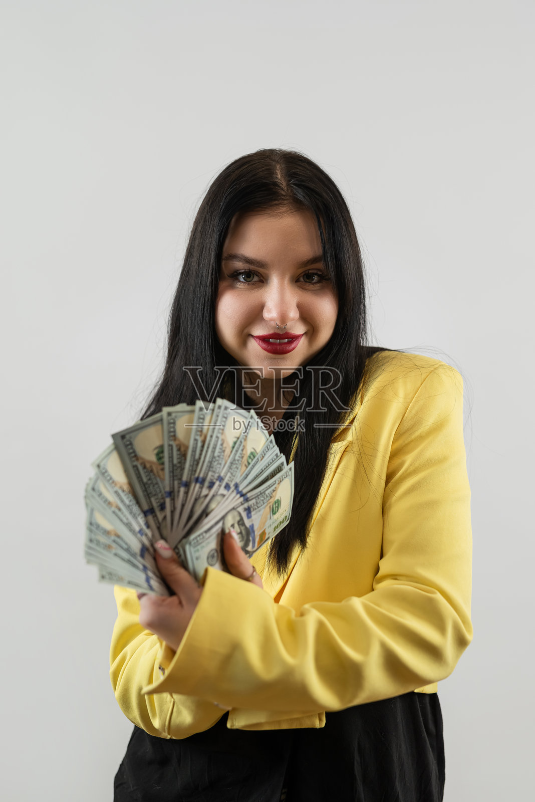 穿着黄色西装的女商人手持美元，背景为灰色。照片摄影图片