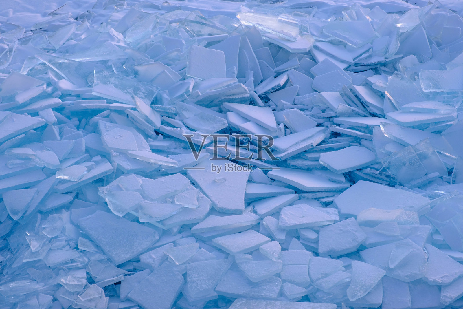 无尽的冰冻贝加尔湖上的雪堆场。寒冷的日子里，蓝色冰块上覆盖着雪的碎片堆。照片摄影图片