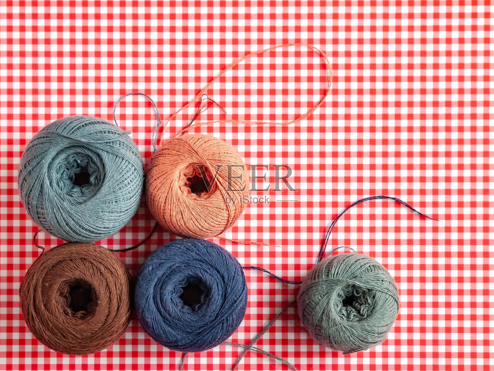 红色格子背景上的多彩棉线卷。选择性对焦照片摄影图片