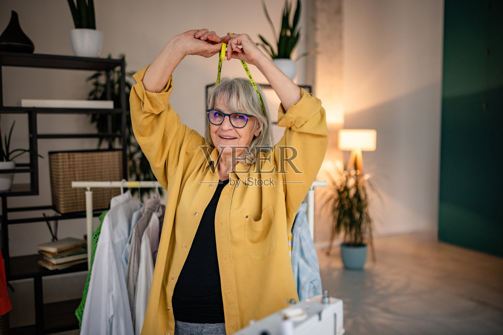 一位年长的女裁缝在她的服装设计工作室里愉快地工作，手中拿着卷尺。照片摄影图片