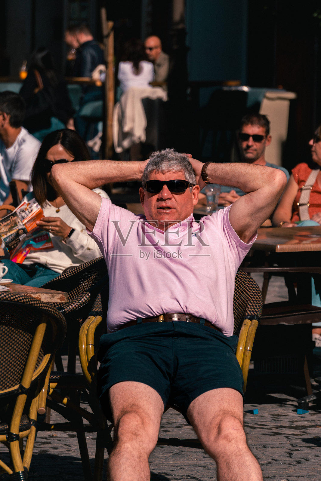 男子在咖啡馆的露台上晒太阳。男子坐在椅子上，双手放在头后，双腿伸展，享受阳光。照片摄影图片
