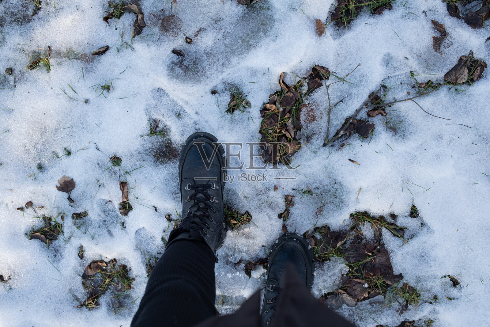穿着靴子的腿站在雪中。照片摄影图片