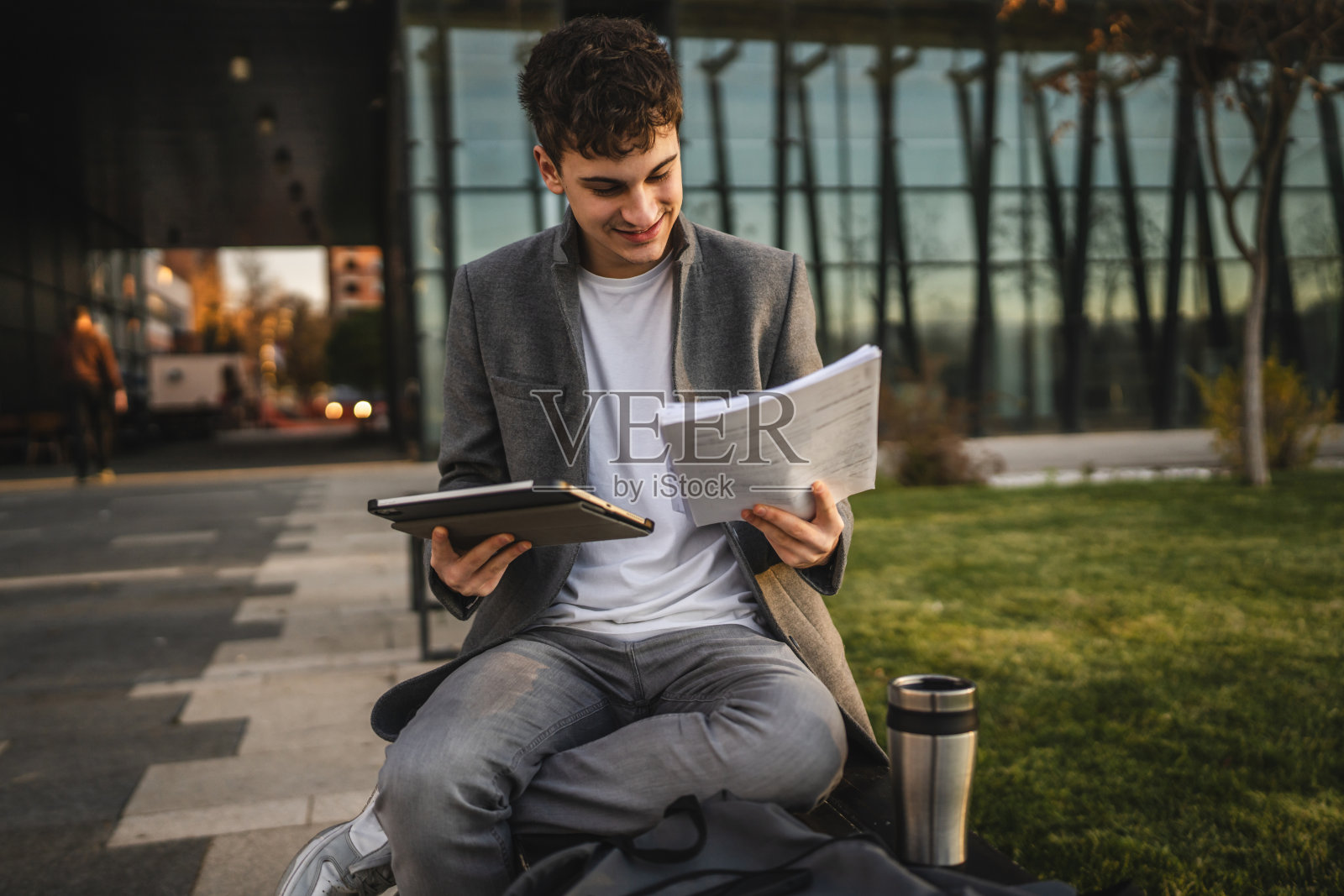 年轻男子坐在长椅上对比平板电脑和文件中的信息照片摄影图片