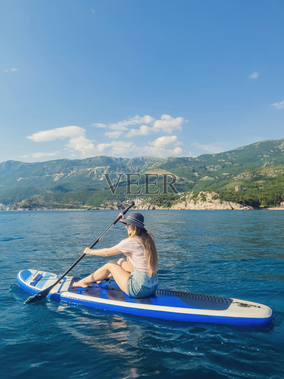 年轻女性在黑山的米洛切尔公园背景下，在圣斯特凡岛附近的蓝色海水中享受立式划水的乐趣。照片摄影图片