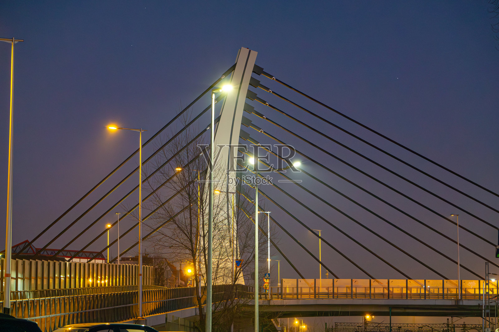 日落时分，公路桥横跨火车站。现代城市建筑在日落时分。夜间桥梁照明。多彩的天空。现代建筑，城市建设。照片摄影图片