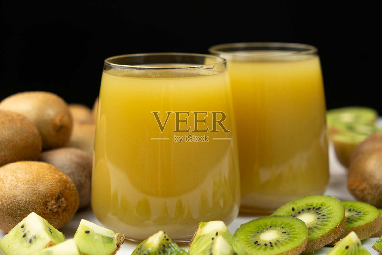 黑色背景下的玻璃杯中盛有猕猴桃汁维生素饮料，周围是新鲜的猕猴桃水果照片摄影图片