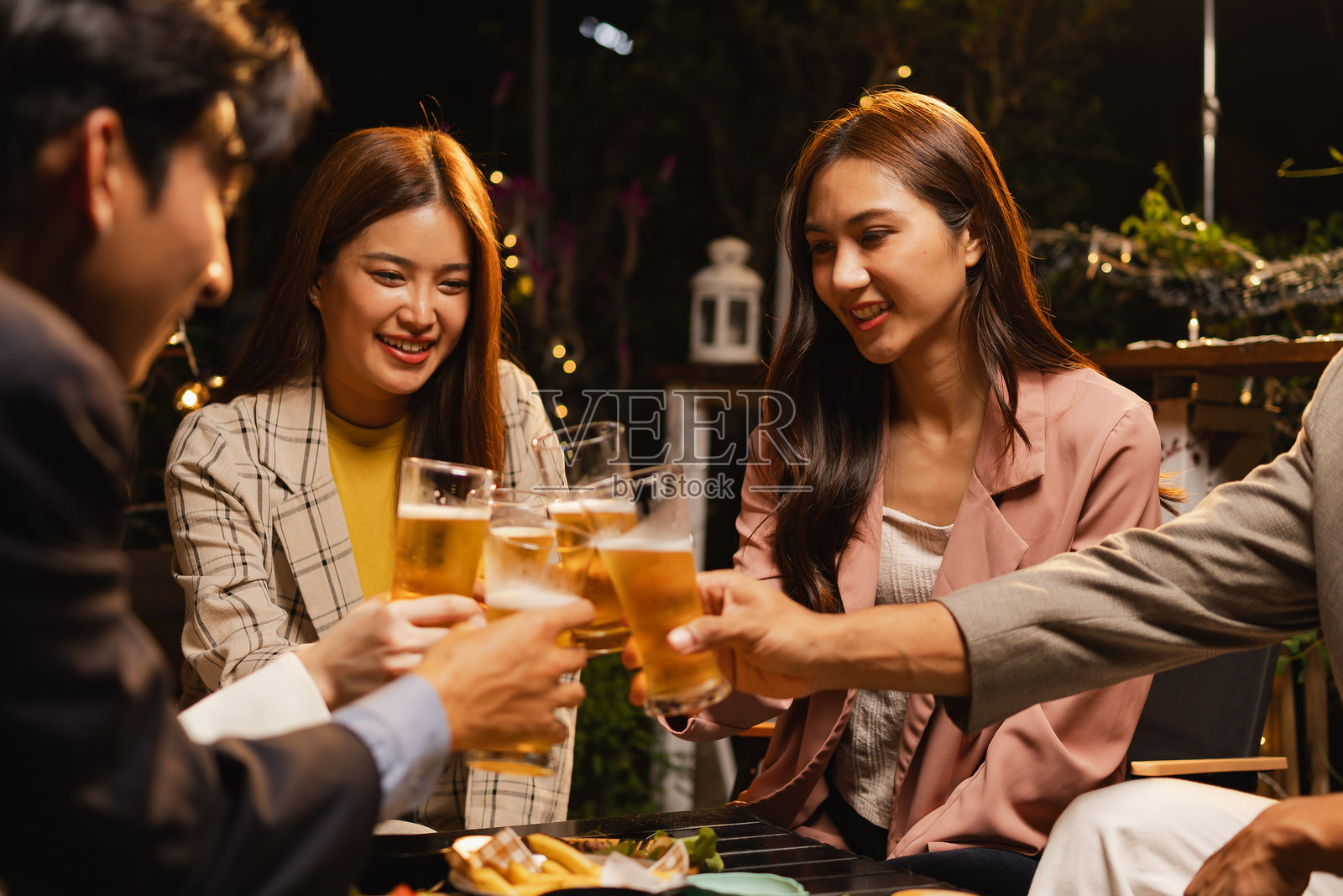 一群朋友在夜晚的庆祝派对上碰杯庆祝。照片摄影图片