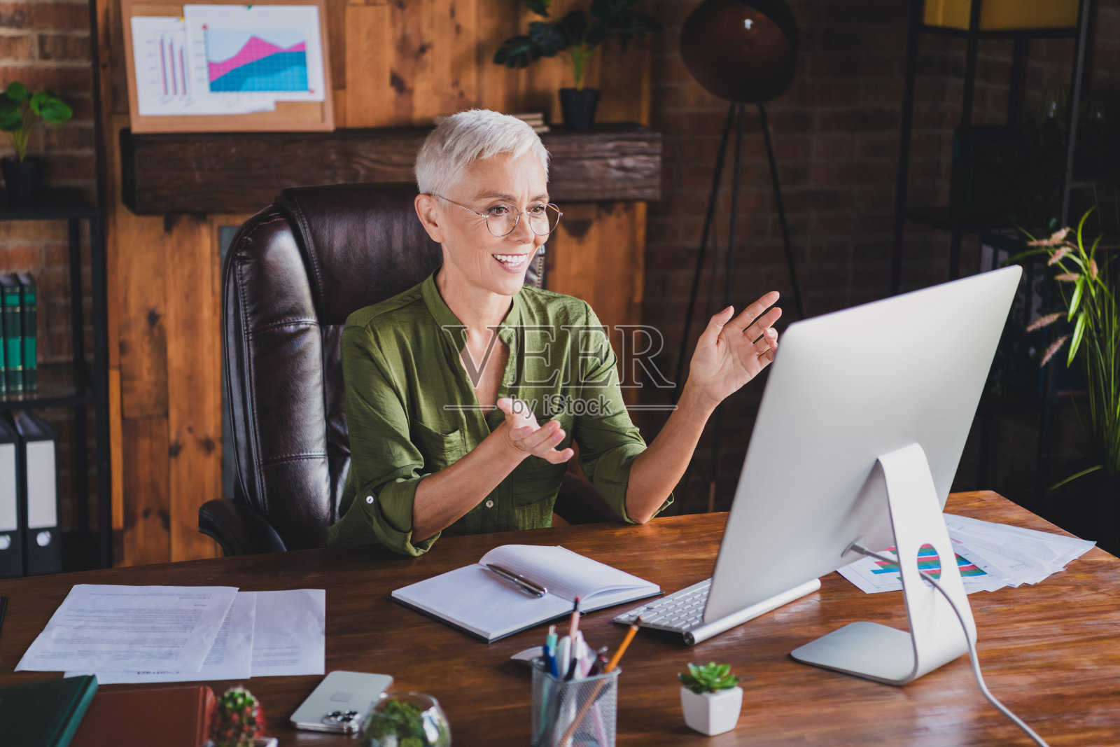 一位年长的企业女性在现代阁楼风格的商务中心办公室内进行视频通话，穿着衬衫。照片摄影图片