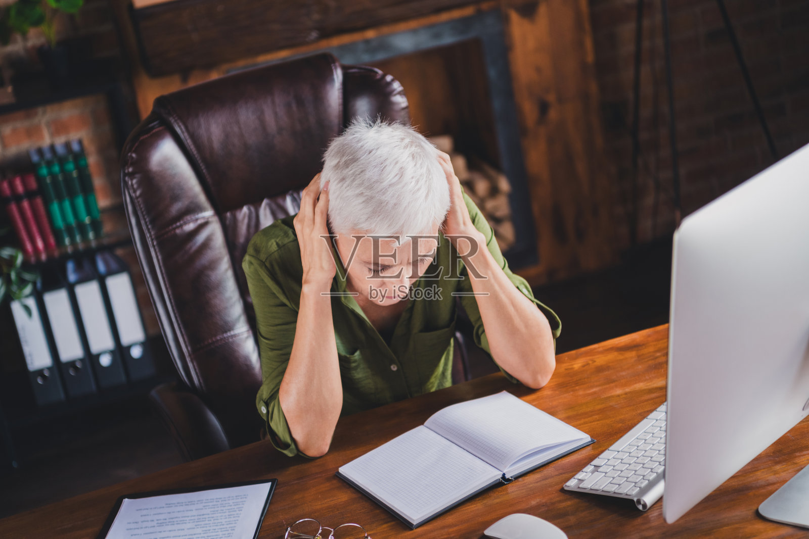 一位迷人的伤心女士穿着衬衫，戴着眼镜，感到疲惫，坐在工作场所的阁楼室内。照片摄影图片