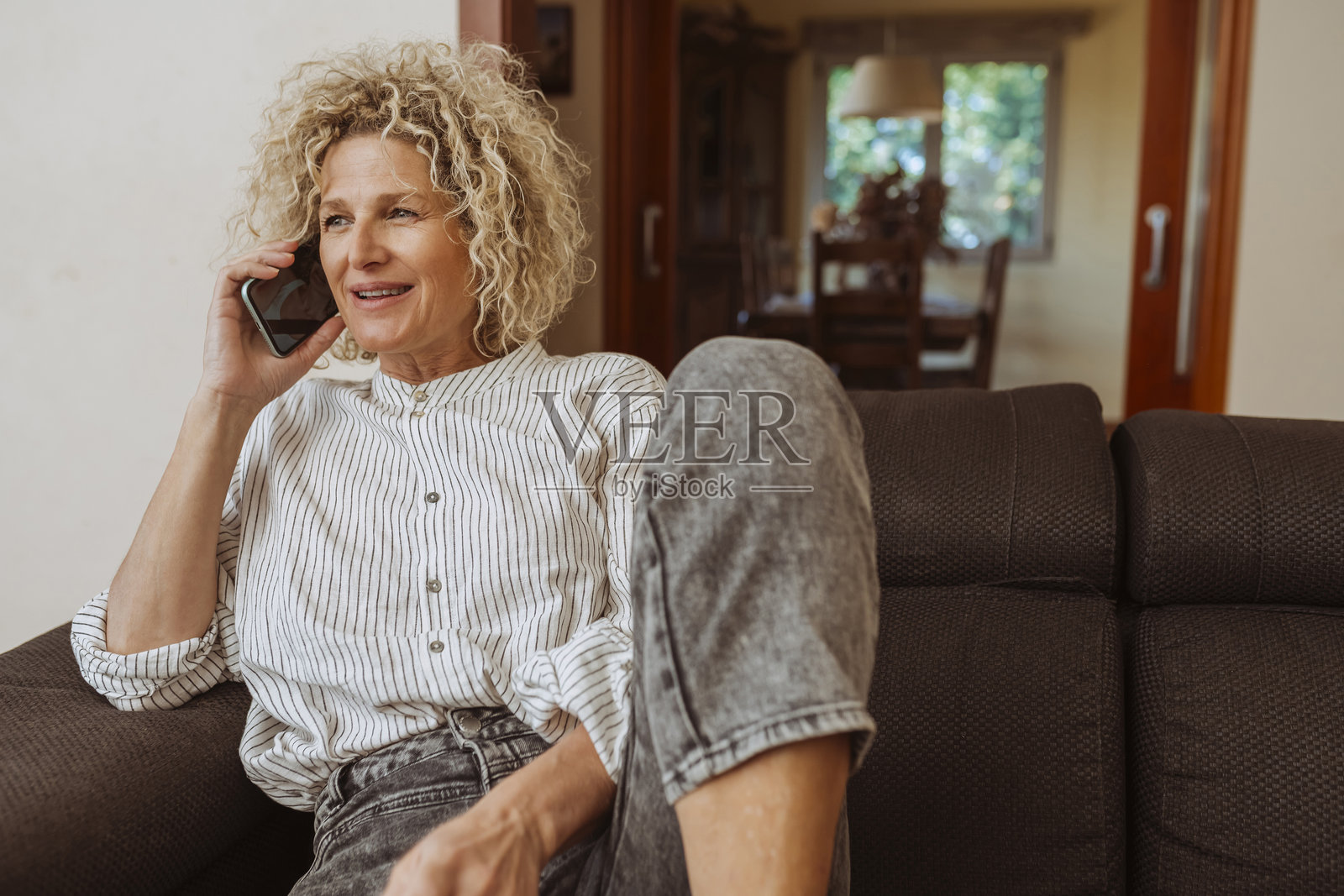 微笑的成熟的女性在家中沙发上放松时使用智能手机交谈照片摄影图片
