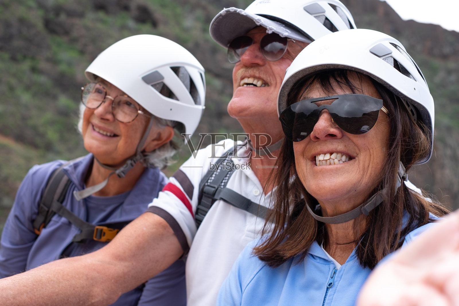 三位快乐的老年朋友戴着保护头盔，一起享受在山上徒步旅行的一天照片摄影图片