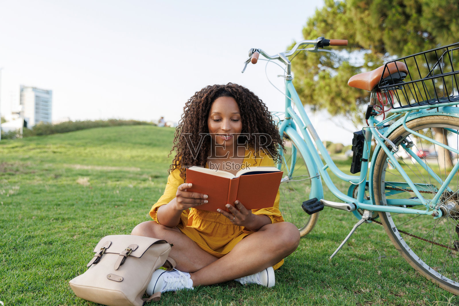 年轻女性坐在公园的草地上，享受阅读一本书，旁边停着她的自行车。照片摄影图片