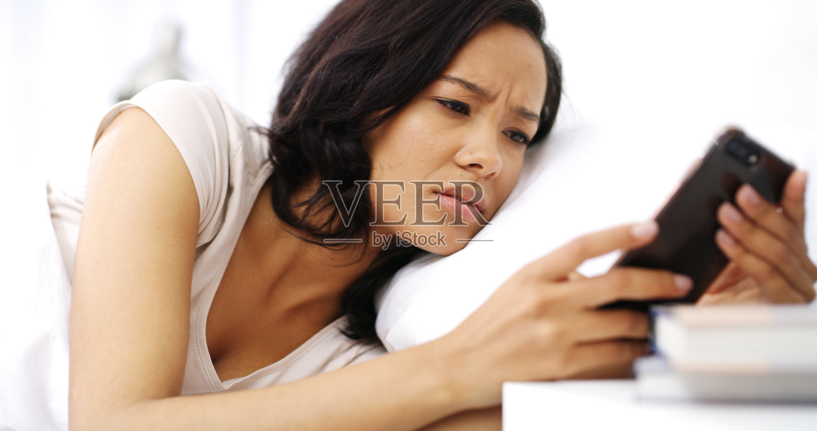 周末早晨，女人在家床上困惑地看着手机，收到分手短信。她在公寓的卧室里感到沮丧、生气，放松地躺着，手里拿着手机，得知了坏消息。照片摄影图片