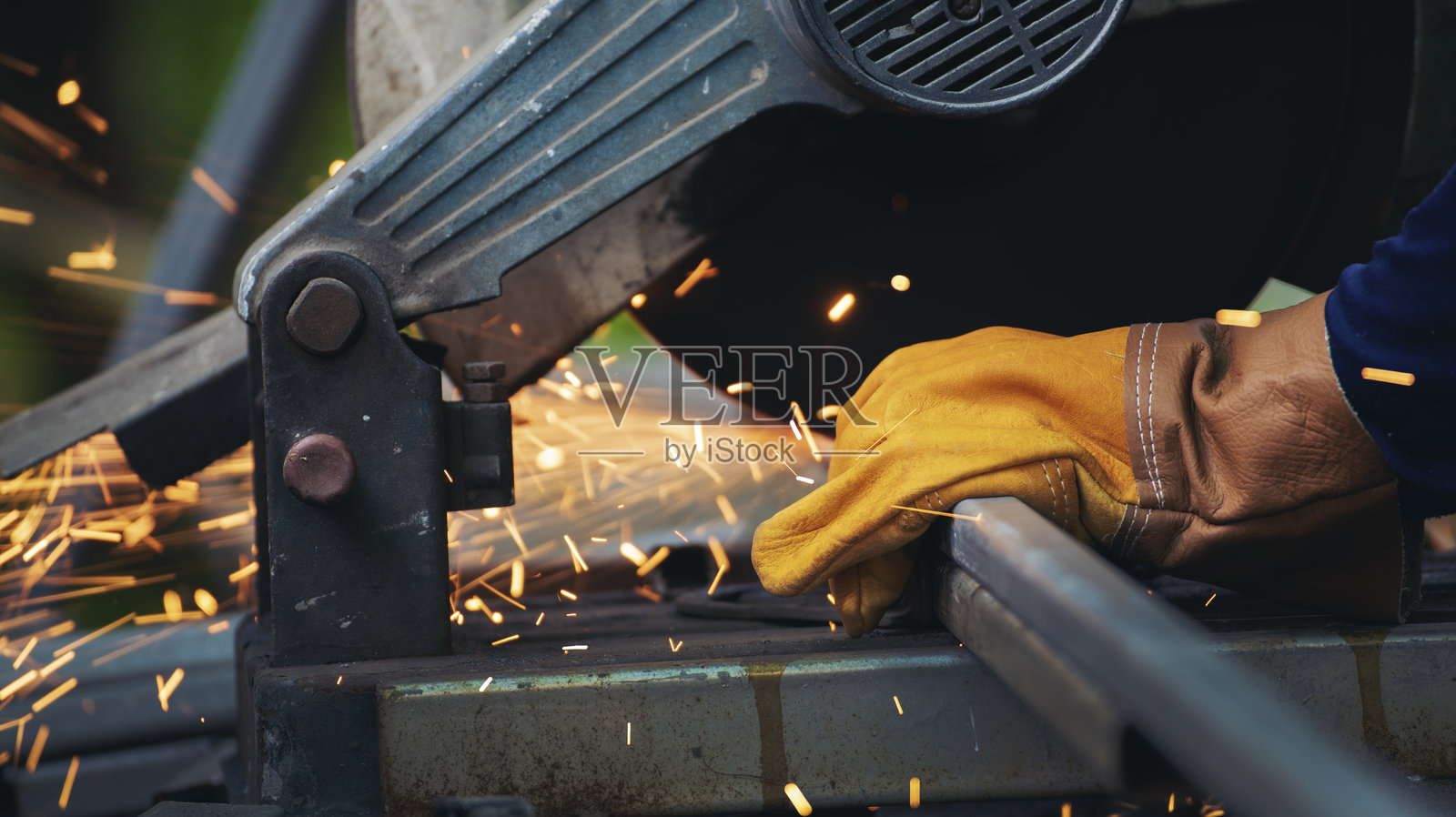 工人手戴着保护手套，焊接机械正在切割铁金属，火花四溅。特写镜头展示了工人在铁匠铺中进行金属加工时的热焰。锁匠焊接机在金属行业中使用。照片摄影图片