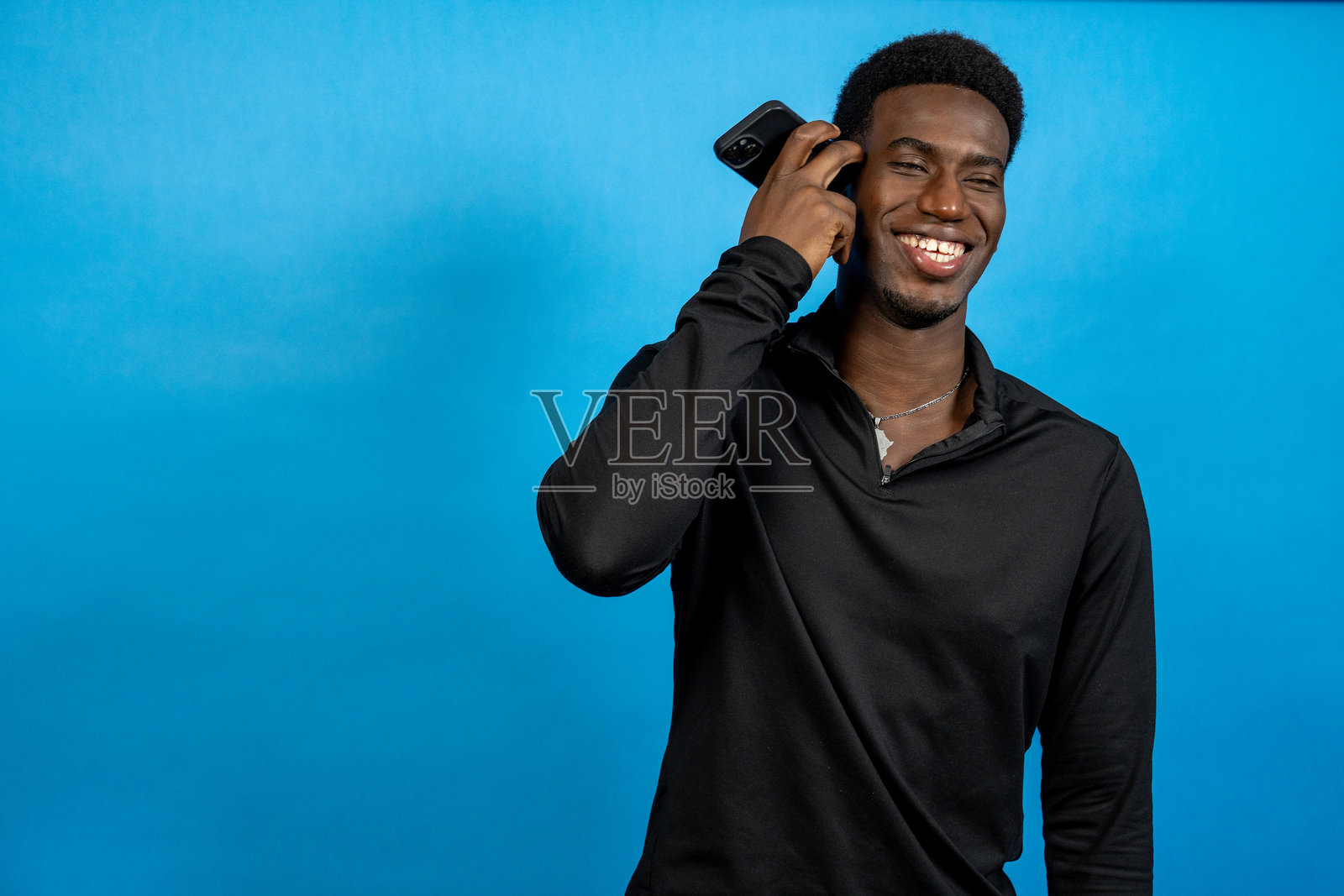 年轻男子微笑着，听着智能手机，背景为蓝色照片摄影图片