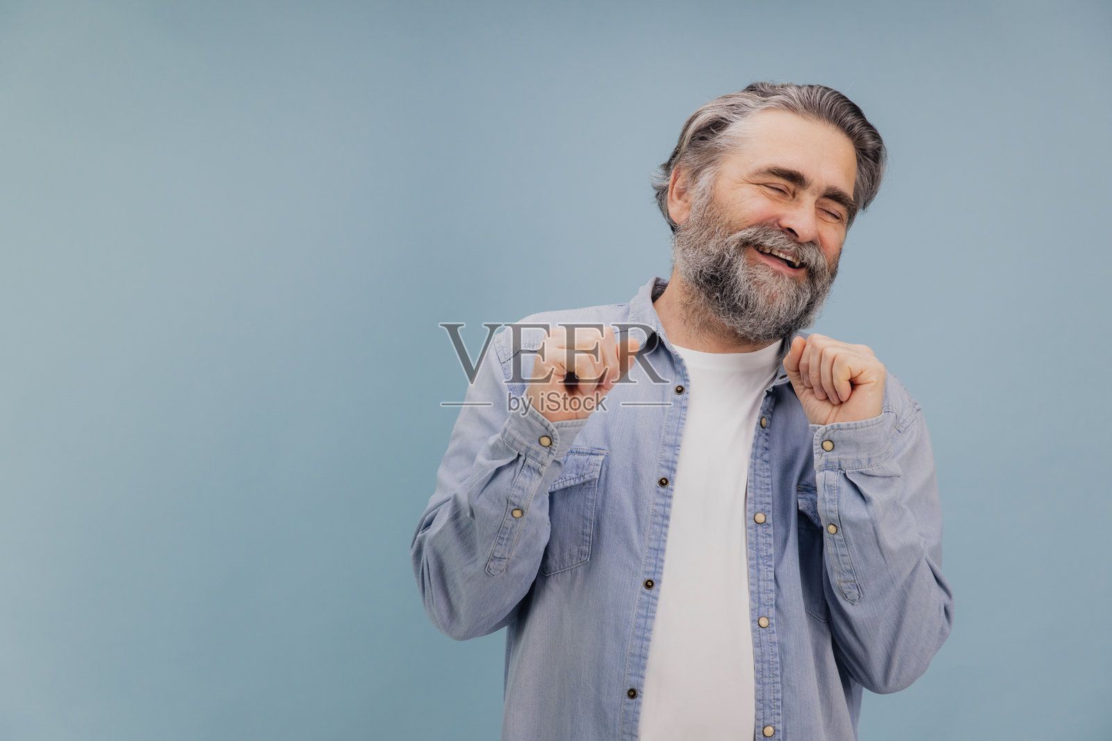 快乐的老年男子在蓝色背景下微笑并整理他的衬衫照片摄影图片