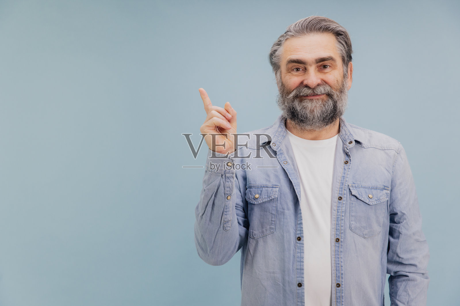 微笑的老年男子在蓝色背景下用食指指向上方照片摄影图片