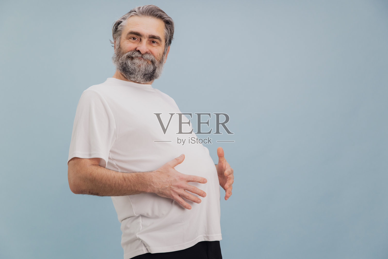 老年男子在蓝色背景下展示大肚子照片摄影图片