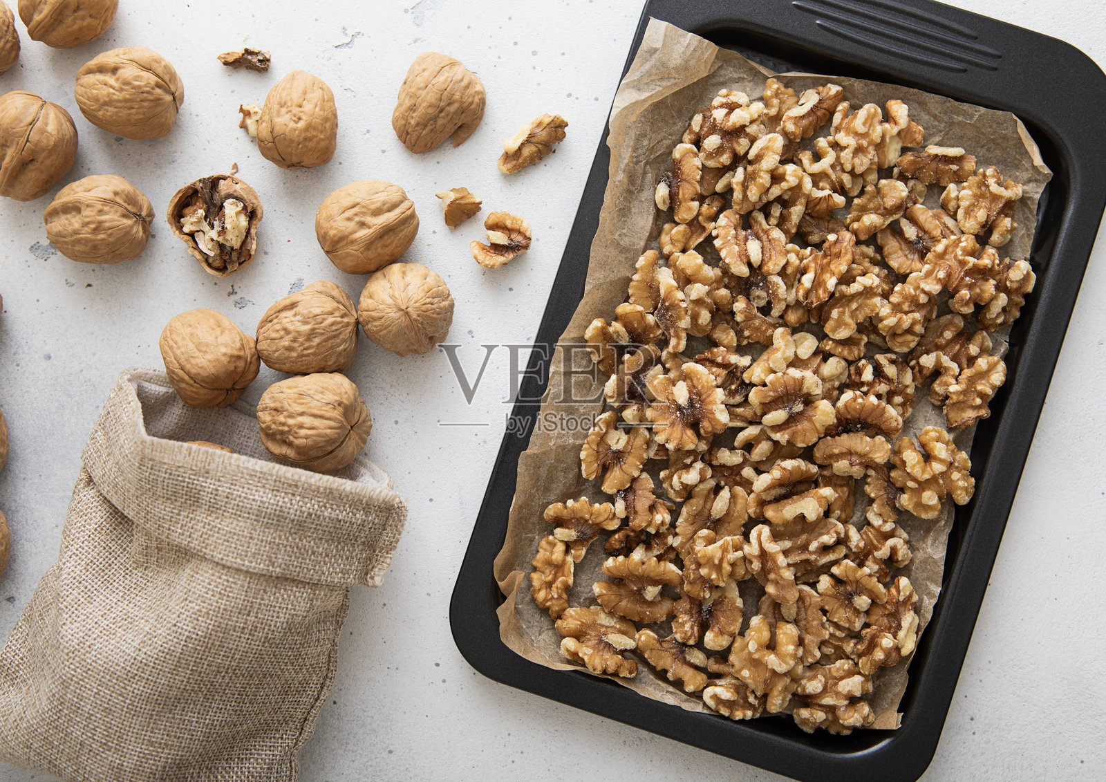 烤盘里放着去皮的生核桃和亚麻袋装的全坚果，背景是浅色的厨房。照片摄影图片