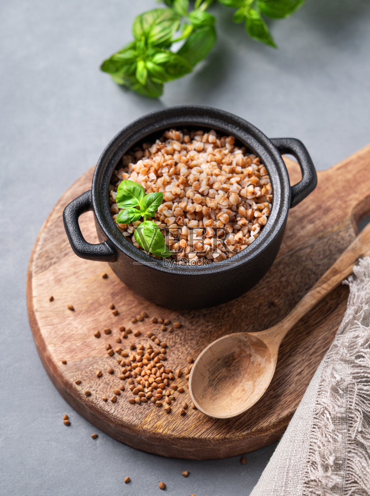 黑锅里的荞麦粥，在浅色背景的砧板上，用生谷物，勺子和新鲜的草药。照片摄影图片