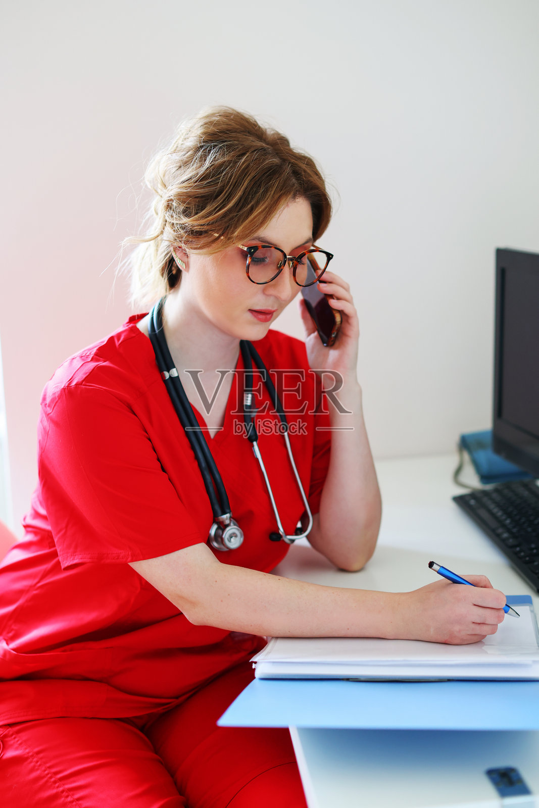 美丽的女医生在电脑前工作和在诊室打电话的画像。照片摄影图片