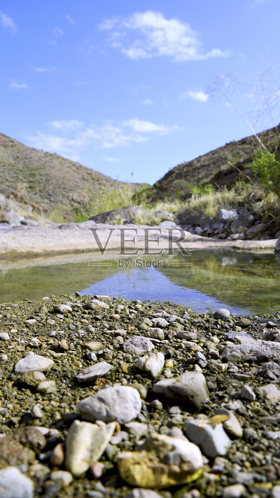 河床的鹅卵石，水坑和贫瘠的山脉在背景中。气候变化概念照片摄影图片