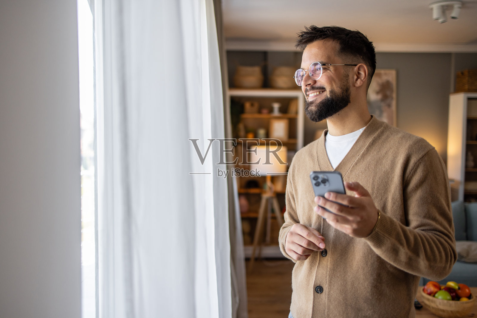 成年男子站在新公寓的客厅里使用智能手机照片摄影图片