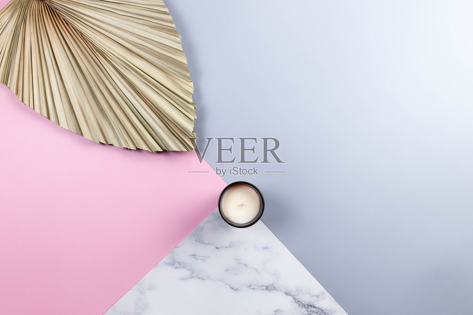 彩色背景上的干棕榈叶和蜡烛的俯视图。蓝色，粉红色和大理石背景。照片摄影图片