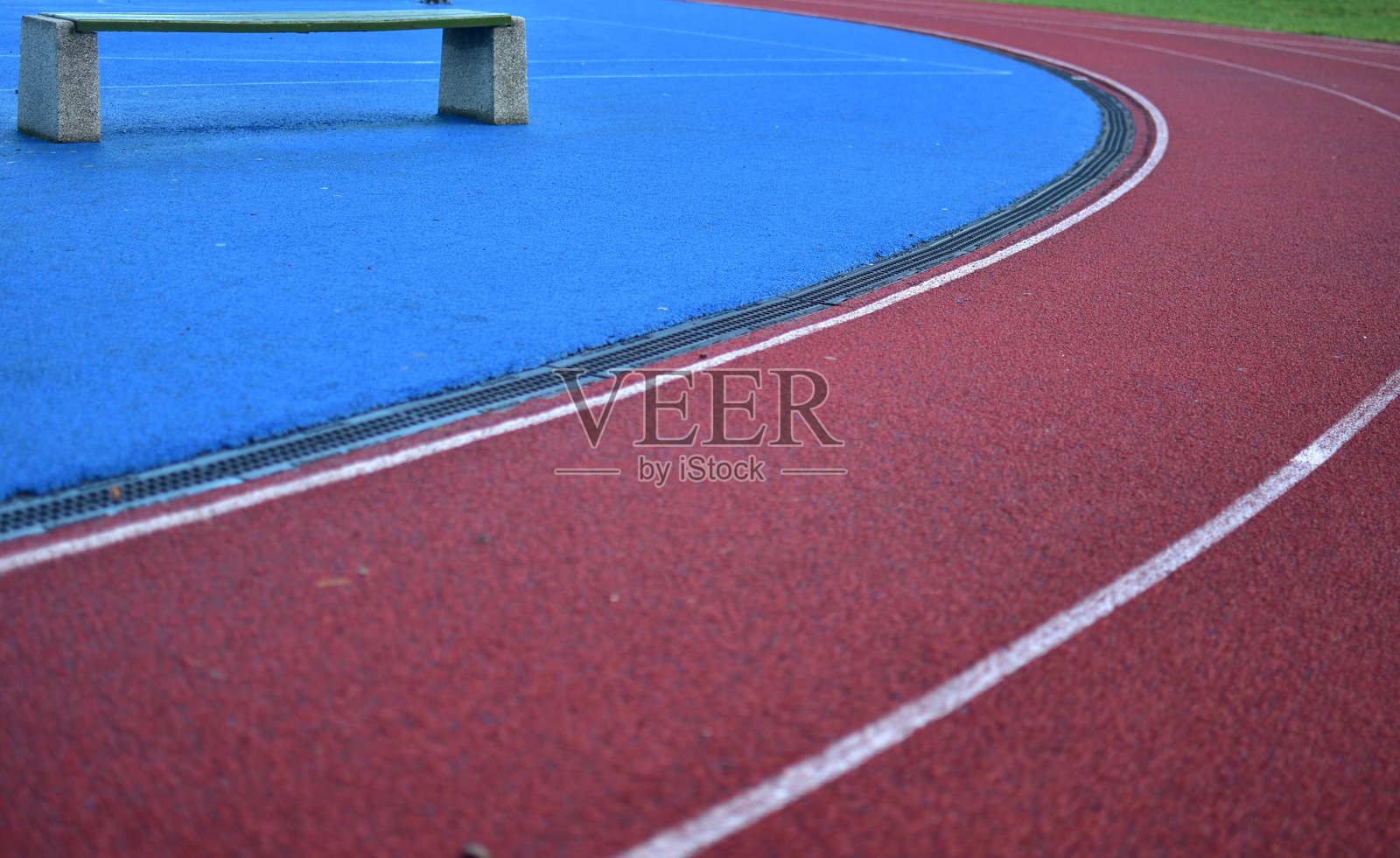红色跑道左侧是蓝色运动场，右侧是绿色草坪，阳光明媚的日子照片摄影图片