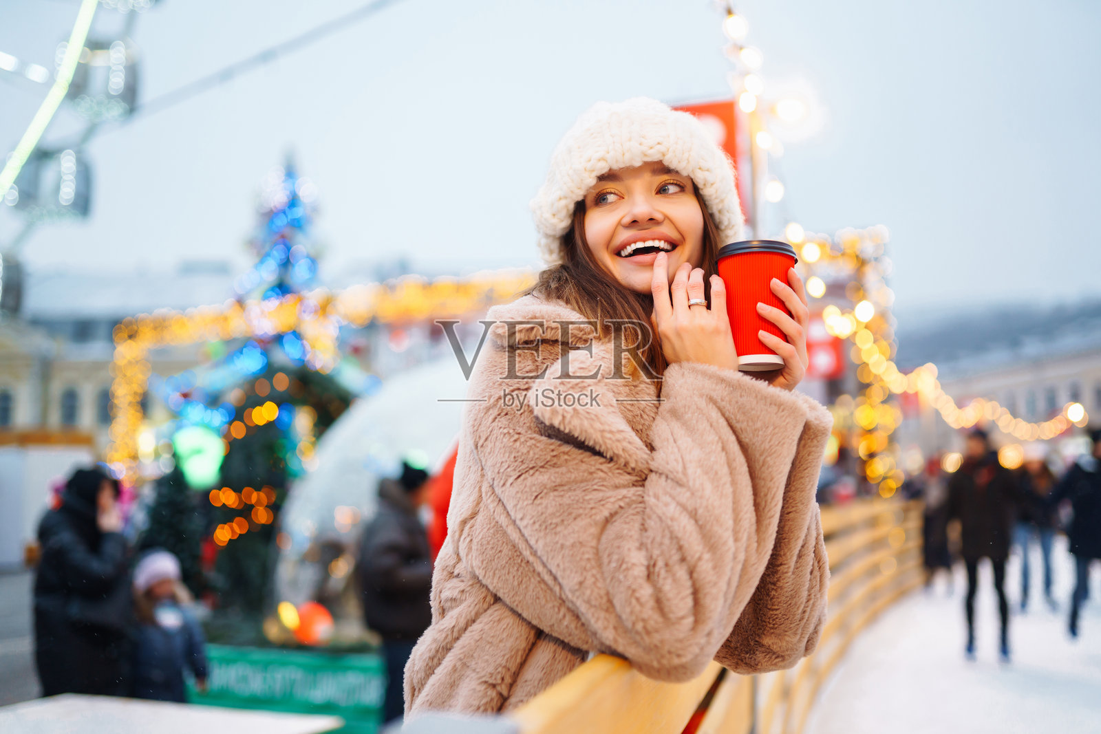 微笑的女性在圣诞市场中走动，手里拿着热咖啡。节日圣诞集市，冬季假日概念。照片摄影图片