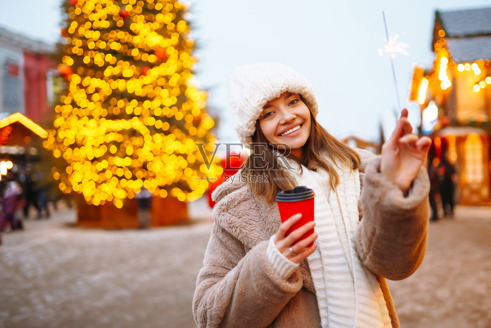微笑的女性在圣诞市场中走动，手里拿着热咖啡。节日圣诞集市，冬季假日概念。照片摄影图片