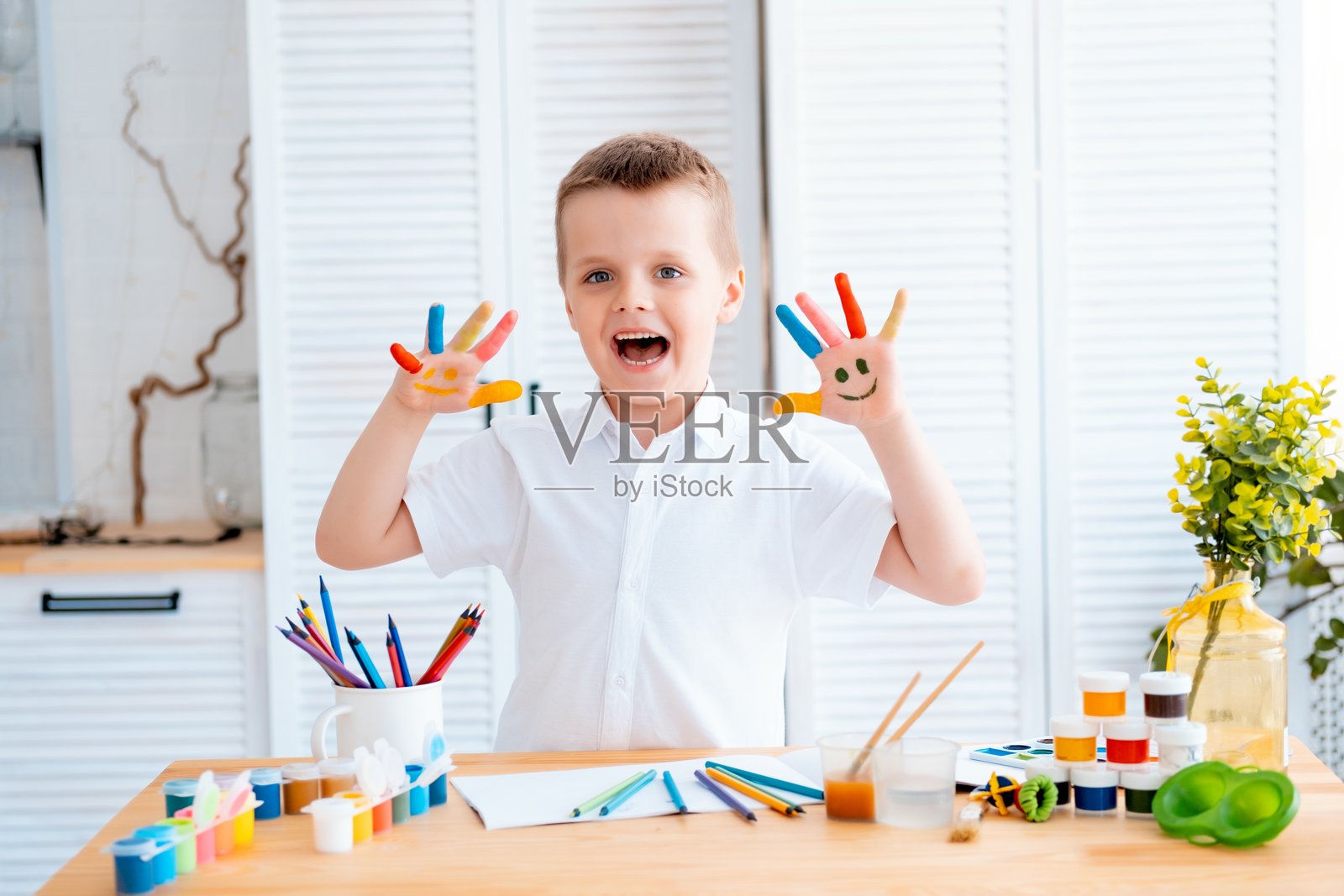 一个小孩在明亮的房间或艺术学校的桌子上用铅笔或颜料画画，快乐的孩子用手或手指学习绘画。照片摄影图片