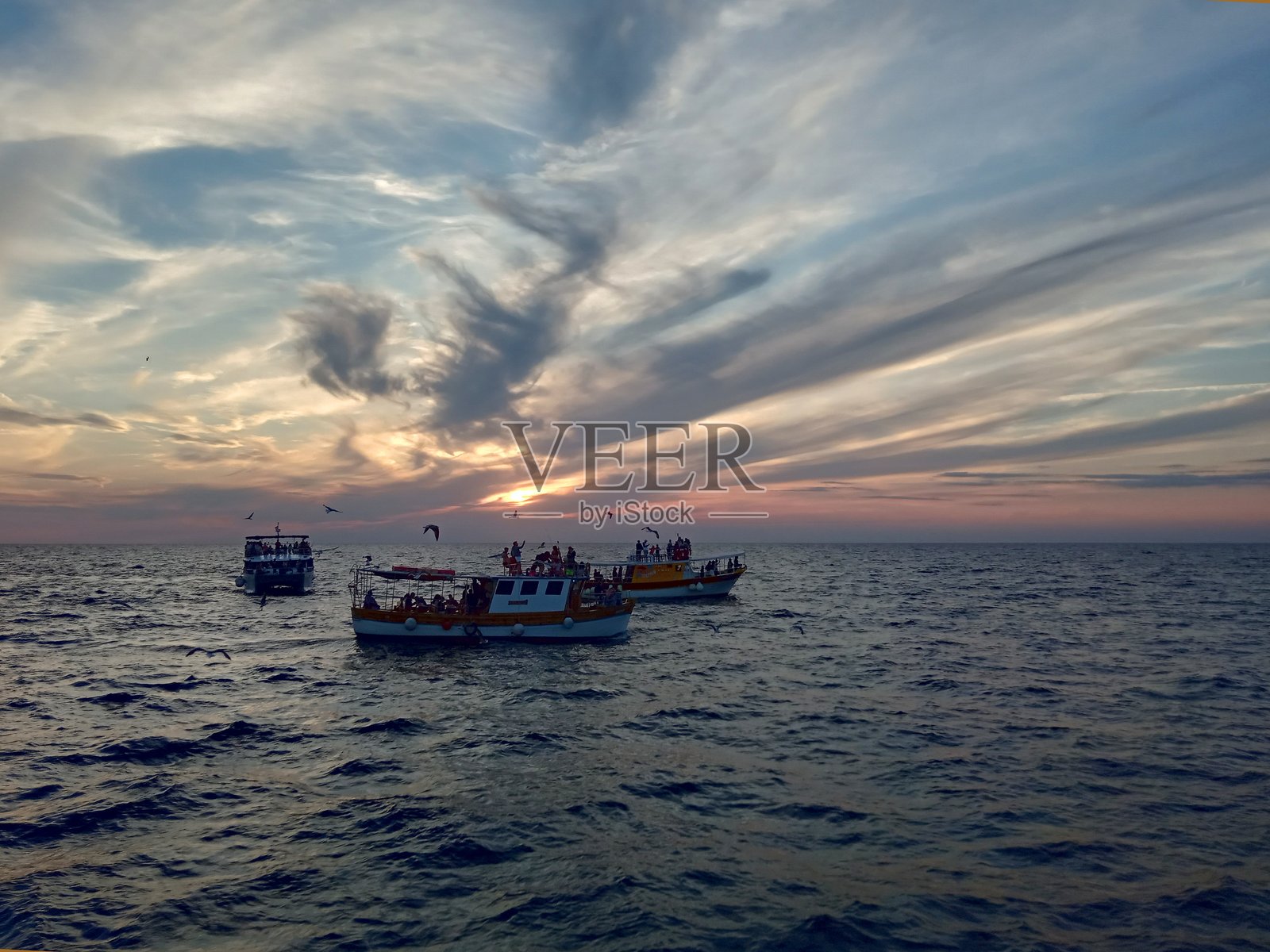 一群人在三艘船上享受海上的日落照片摄影图片