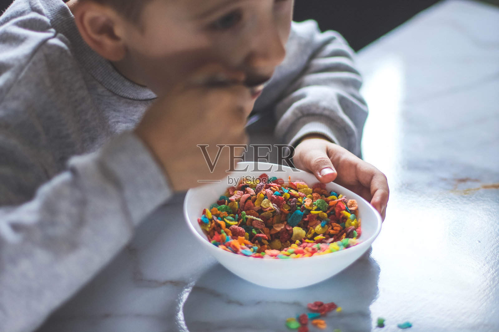 男孩在早餐时从盘子里吃五颜六色的干麦片。照片摄影图片