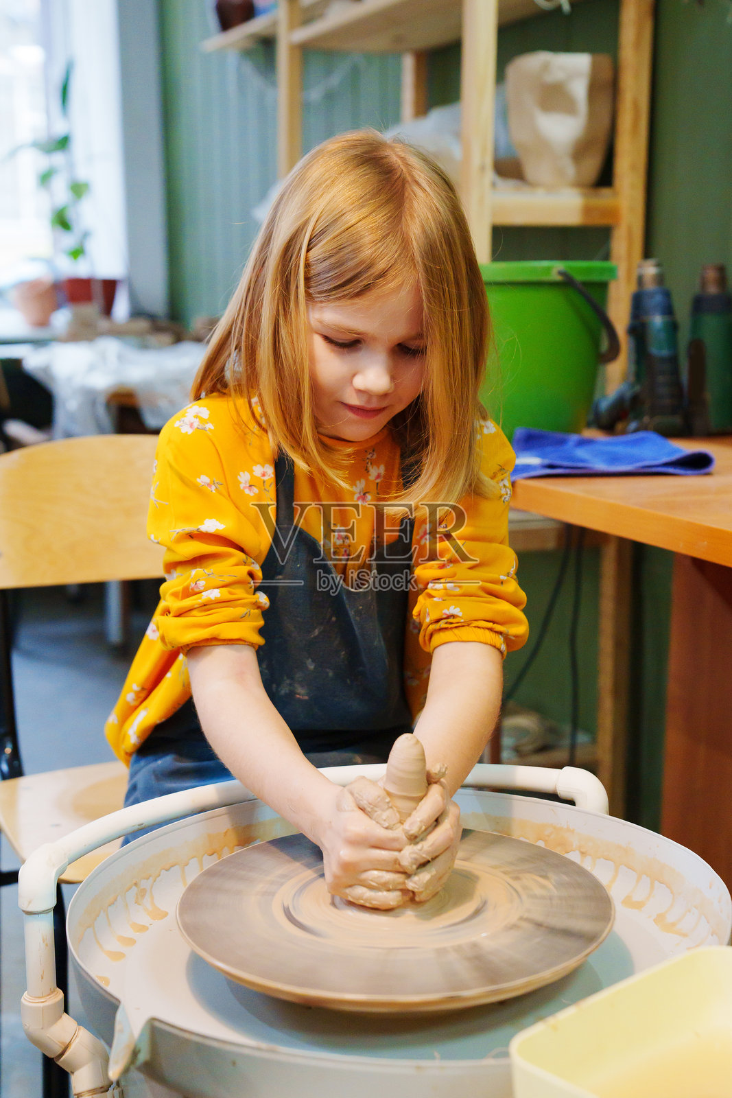 一个金发少女在陶轮上用粘土雕刻。照片摄影图片