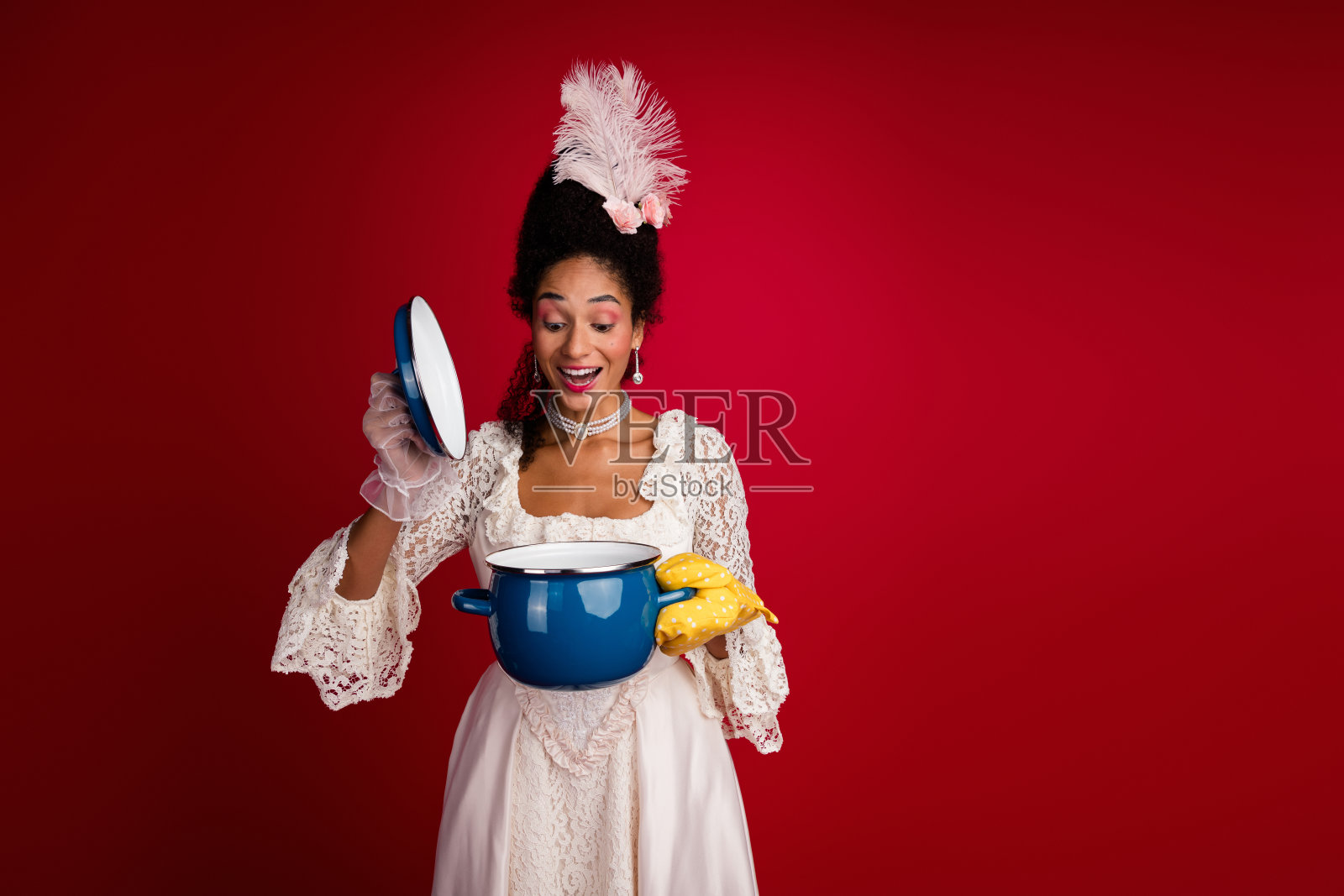 优雅着装的年轻女性在红色背景下的锅中发现惊喜，融合了历史服饰与现代元素。照片摄影图片