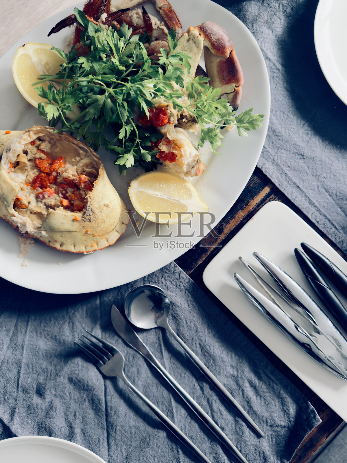 一盘准备好的螃蟹，配有柠檬和香草，摆放在餐桌上。照片摄影图片