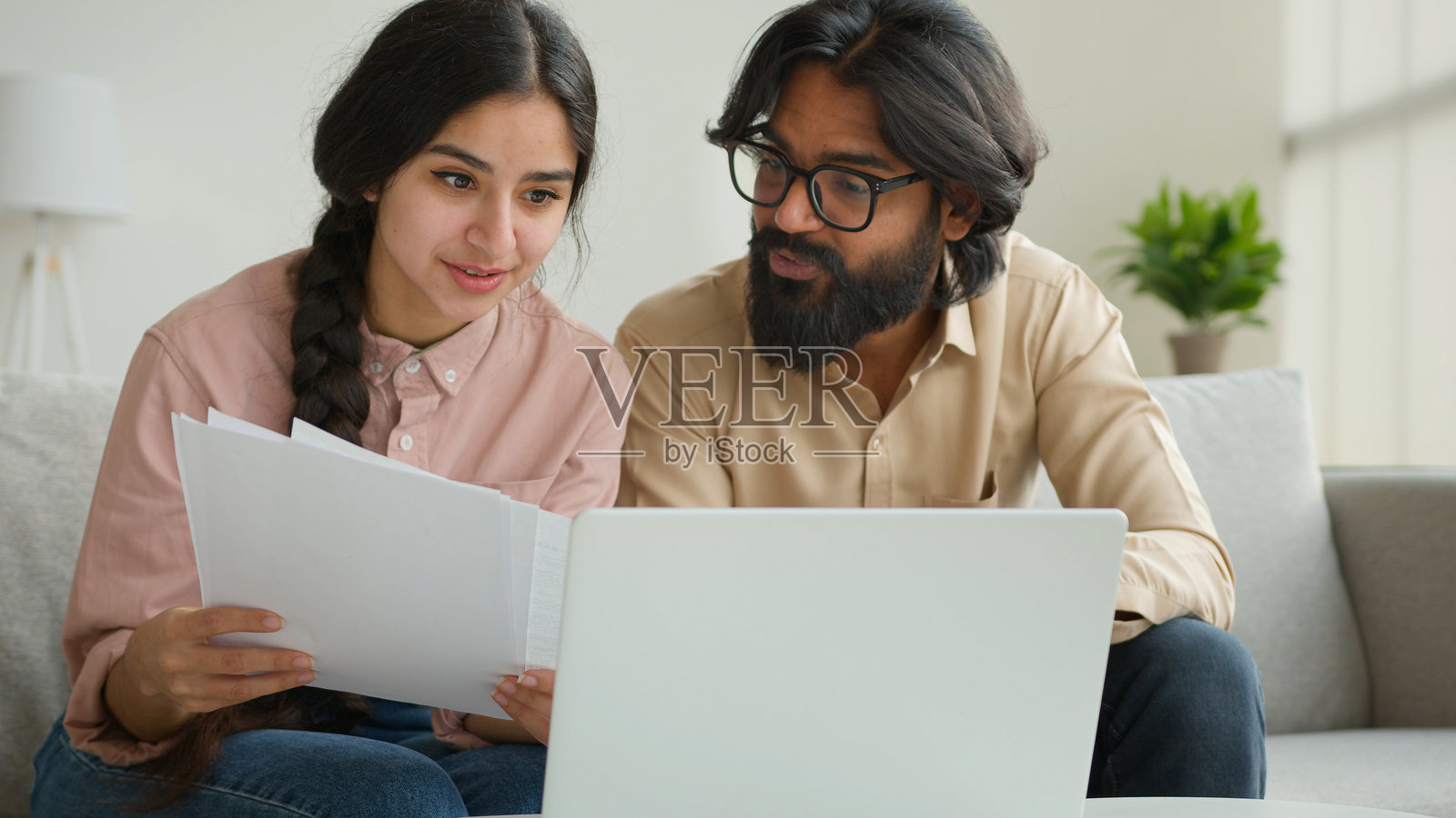 阿拉伯夫妇在家中阅读租赁文件，在线支付家庭账单和税款，跨民族的男女正在讨论预算，谈论贷款文件和房屋抵押贷款。照片摄影图片