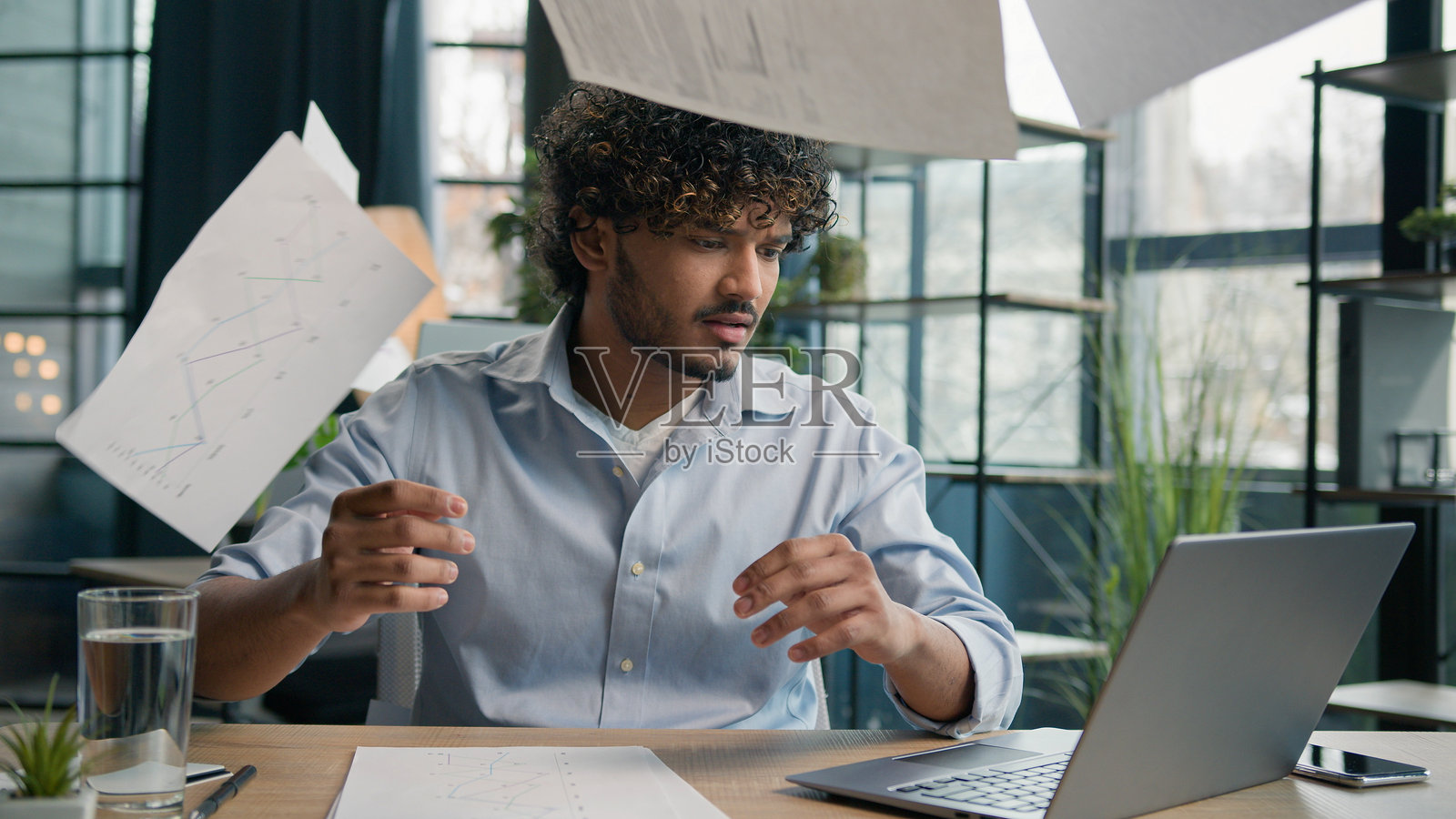 在办公室里感到压力巨大的阿拉伯印度男子，因工作失败而愤怒疲惫，面临文件问题和困难任务，烦恼地扔掉纸张，因商业错误而感到疲惫不堪。照片摄影图片