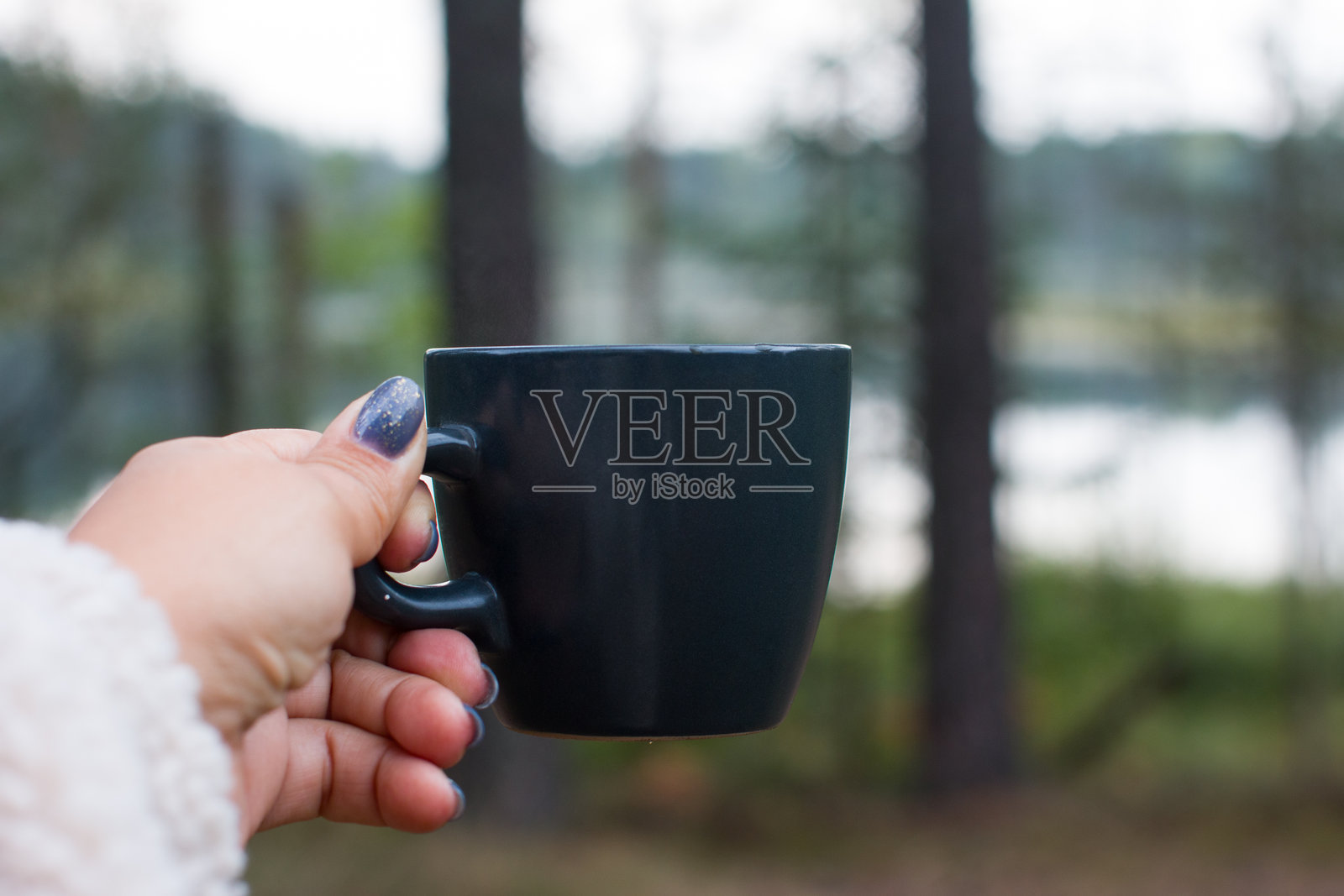 一只女性的手握着一杯热饮，背景是自然风光。照片摄影图片