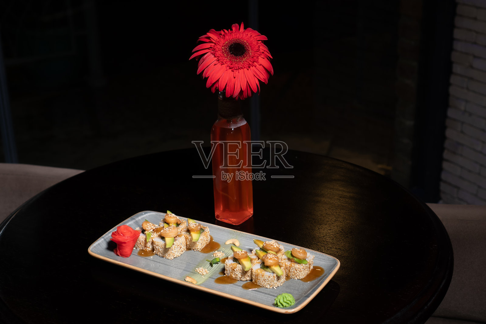 特写:餐厅里，用米饭、金枪鱼、鳄梨、虾、黄瓜、芝麻酱做成的寿司，放在一个矩形盘子里，桌子上放着一朵花，上面放着姜和芥末照片摄影图片